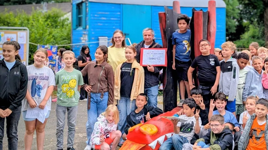 Nach fünf Projekttagen ist der freundliche Drache „Hugo“ fertig:
Gemeinsam mit dem Bamberger Bildhauer Thomas Gröhling
präsentieren die Schülerinnen und Schüler der Hugo-vonTrimberg-Grundschule das neue Kunst- und Spielobjekt auf
ihrem Pausenhof. (Foto: Juliane Renninger, Bildungsbüro Stadt
Bamberg)